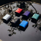 Six colorful vape pods arranged on reflective surface, showcasing red, blue, green, silver, black, and purple options