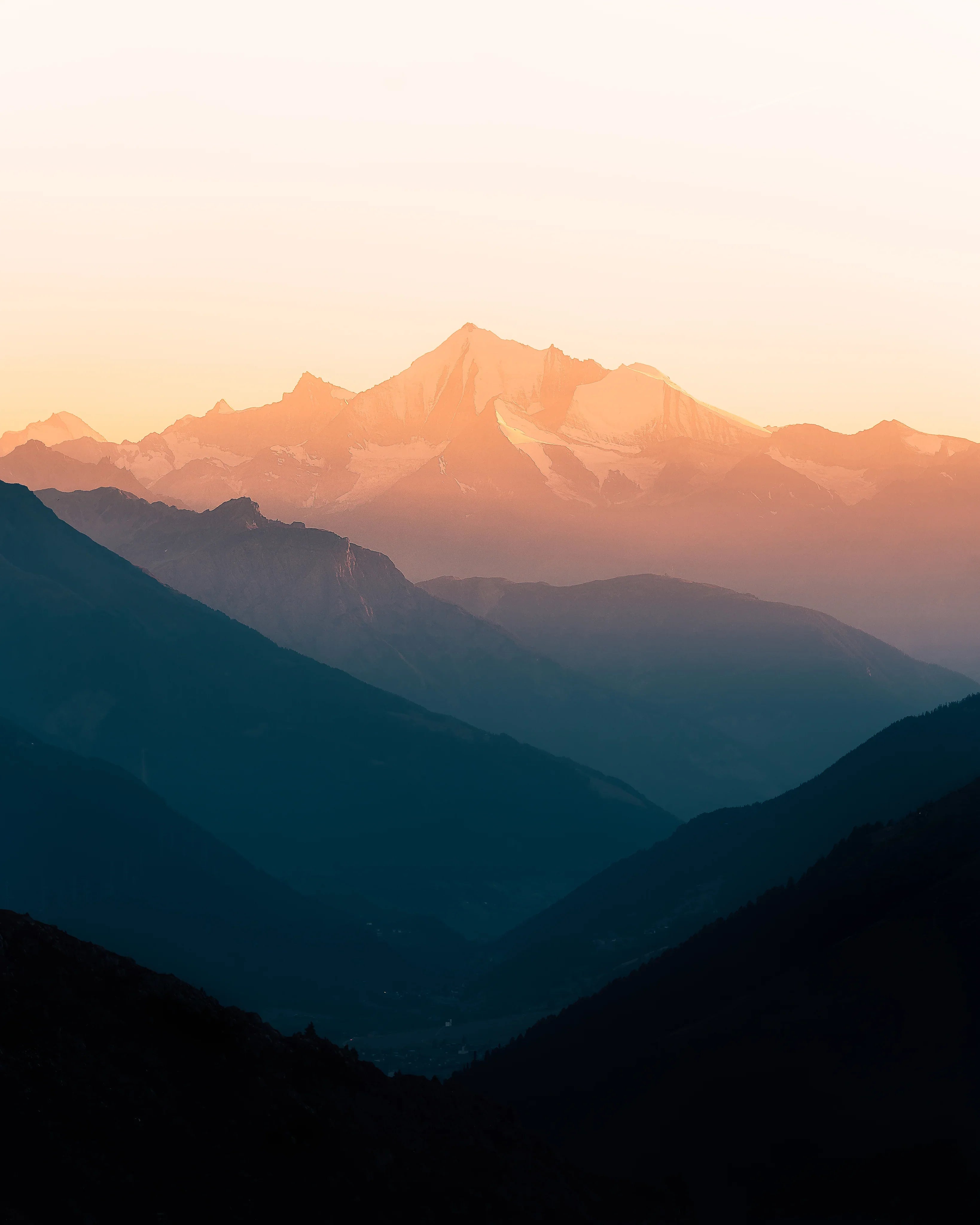 Sunset over snow-capped mountain peaks with layered valleys below