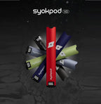 Syokpod V2 disposable vape pens in red, blue, green, and black with 100 puff count on dark cracked background
